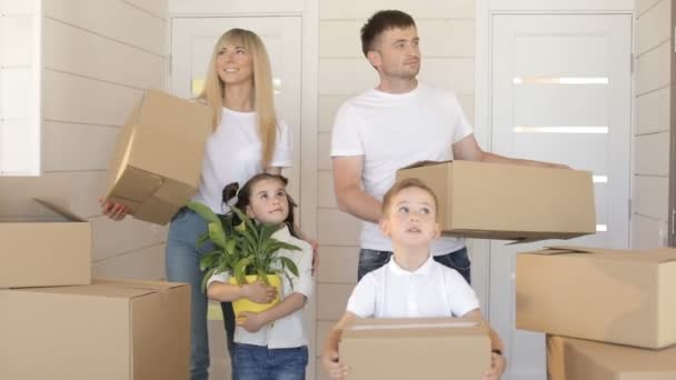 Familie verhuizen naar een nieuw huis. Jonge exaciting familie uitvoering kartonnen doos in het nieuwe moderne huis naar de woonkamer. Gelukkige familie met kartonnen dozen in nieuw huis — Stockvideo