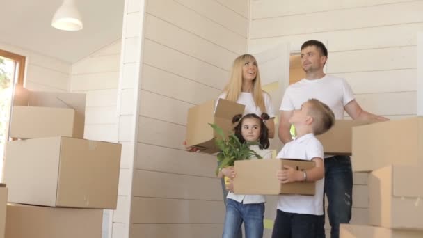 La familia se muda a un nuevo hogar. Joven familia exacitante llevando caja de cartón en el nuevo hogar moderno de la sala de estar. Familia feliz con cajas de cartón en casa nueva — Vídeos de Stock
