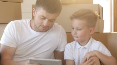 Baba ve oğul kutuları backgroud, yeni daire, tablet bilgisayarda oynama ile portresi. İpotek, hareketli ve gayrimenkul konsept.