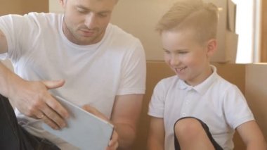 Baba ve oğul kutuları backgroud, yeni daire, tablet bilgisayarda oynama ile portresi. İpotek, hareketli ve gayrimenkul konsept.