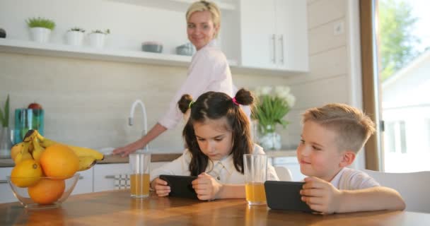 Moeder en kinderen samen op keuken. Portret van klein schattig meisje en jongen is met behulp van slimme telefoon terwijl moeder is het maken van sap drinken. Familie concept — Stockvideo