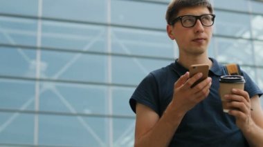 Akıllı telefon kullanarak ve Havaalanı zemin üzerine kahve içme gözlüklü genç adam portresi.