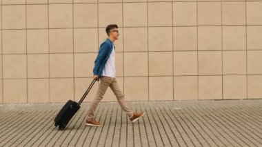 Şık genç adam akıllı telefon yazarken terminal Havaalanı'na yürüyüş bagaj ile rahat gömlekli.