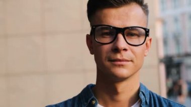 Kameraya bakarak ve şehir arka plan üzerinde gülümseyen gözlüklü genç çekici adam portresi kapatın.