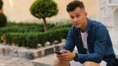 Şehirde sokakta arkadaşlarınızla sohbet, kameraya dönüm ve gülümseyen cep telefonu kullanan yakışıklı adam. Yan görünümü. Görünümü kapatın.