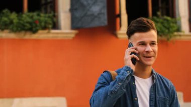 Şehirde sokakta cep telefonuyla konuşan genç yakışıklı adam görüntüsünü kapatın. Yan görünüm.