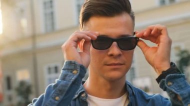 Fotoğraf makinesi üzerinde güneş gözlüklü ve şehir arka plan üzerinde gülümseyen genç çekici adam portresi.