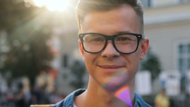 Close up portrait of young attractive man in the glasses looking to the camera and smiling in the city on the sunset background. — Stock Video