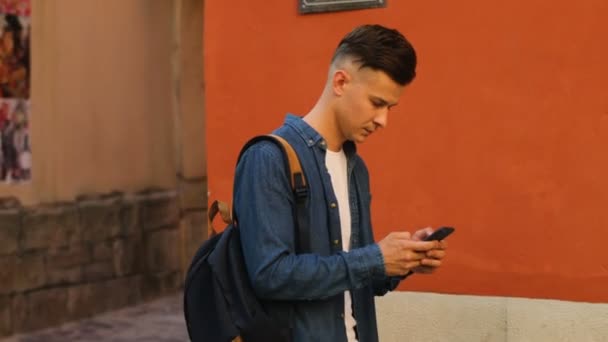 Hombre guapo usando el teléfono celular para charlar con amigos en la calle de la ciudad. Vista lateral . — Vídeos de Stock