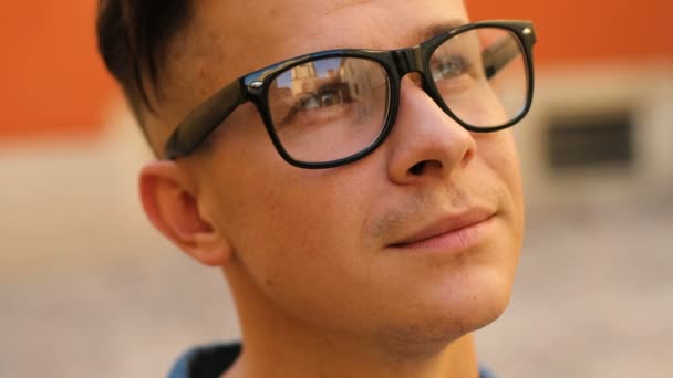 Крупный план портрет молодого стильного человека в очках в городе на фоне оранжевой стены . — стоковое видео