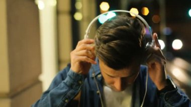 Akşam ve başlangıç müzik dinleme, şehirde sokakta yürürken baş telefonları giyen genç adam portresi.