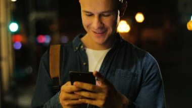 Çekici bir adam akıllı telefon sokakta akşam zaman şehirde kullanarak kot gömlek.