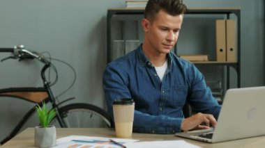 Modern ofis çalışma, kahve içme ve dizüstü bilgisayar kullanma genç iş adamı.