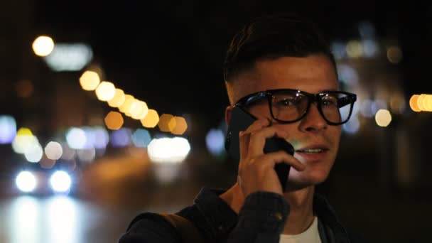 Nahaufnahme eines jungen emotionalen Mannes, der nachts in der Stadt mit dem Smartphone spricht. Seitenansicht. — Stockvideo