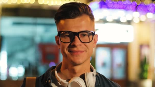 Portrait de jeune homme élégant dans les lunettes avec casque dans la ville à l'heure du soir. Gros plan . — Video