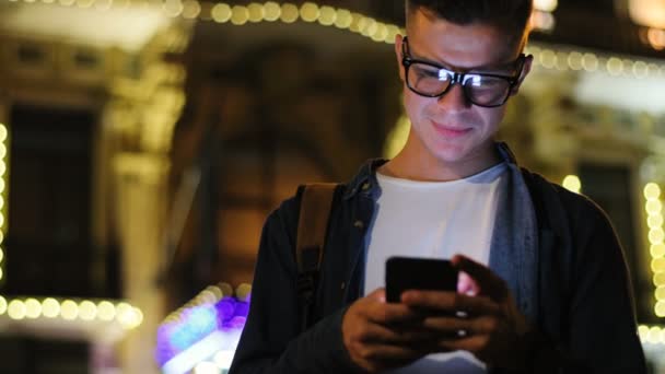 有吸引力的人在时尚的眼镜使用智能手机在街上聊天在晚上时间 — 图库视频影像
