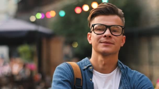 Portrait d'homme heureux dans les lunettes regardant vers la caméra et souriant dans la ville. Plan extérieur . — Video