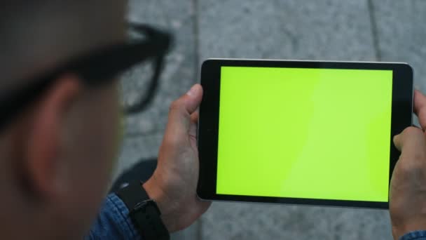 Z bliska strzał atrakcyjne człowieka za pomocą tabletu z zielonego ekranu, siedząc w mieście. Kluczowanie. Pozycji poziomej. — Wideo stockowe