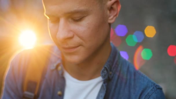 Retrato de un hombre joven y elegante en el centro de la ciudad por la noche durante la puesta de sol con bokeh. Primer plano. . — Vídeo de stock