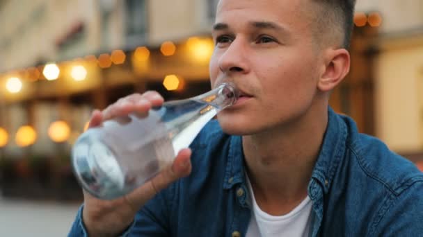 Portrét atraktivní muž pitné vody z láhve na pozadí města. Detailní záběr záběr. — Stock video