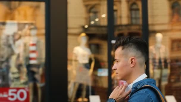 Portret van de jonge man hoofd telefoons te dragen terwijl het lopen op de straat van de stad. Uitzicht vanaf de kant. — Stockvideo