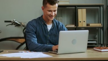 Genç iş adamı şık ofis içinde belgili tanımlık laptop çalışma, iş günü bitirme ve çok mutlu hissediyorum rahat gömlekli.