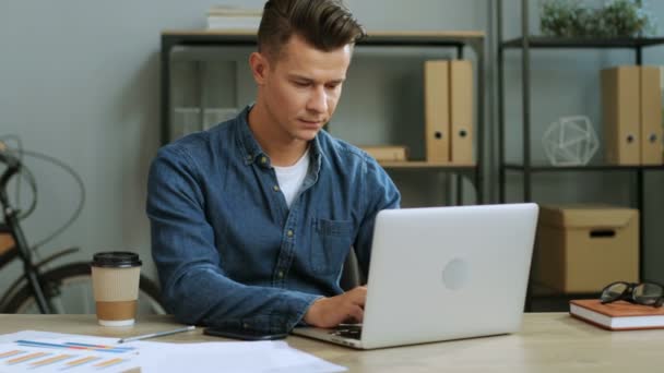 Portret van ernstige jonge zakenman in de glazen in de moderne kantoren met behulp van zijn laptop werkt. — Stockvideo