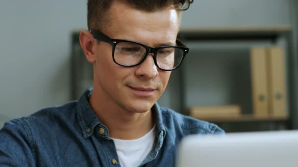 Ritratto ravvicinato di bel giovane uomo d'affari negli occhiali che lavorano sul computer portatile nell'ufficio elegante . — Video Stock