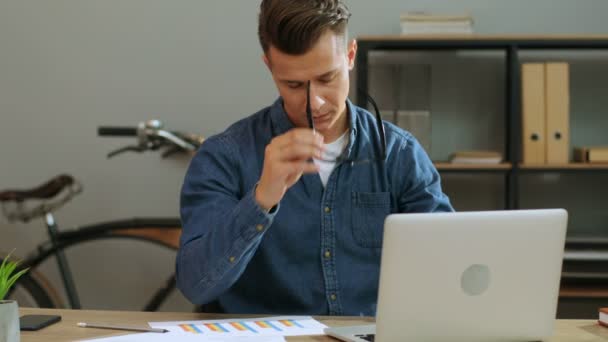 Joven hombre de negocios con camisa casual trabajando en el portátil en la oficina con estilo, sintiéndose muy cansado después del día de trabajo . — Vídeos de Stock