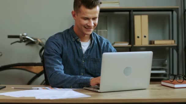 Молодой бизнесмен в повседневной рубашке работает в ноутбуке в стильном офисе, заканчивает рабочий день и чувствует себя таким счастливым . — стоковое видео