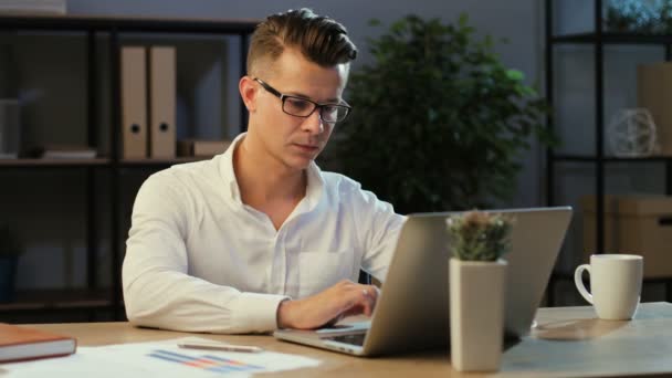 Attractive young business man in the glasses working in the modern office using laptop at the evening. — Stock Video