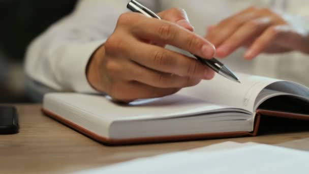 Крупный план человека, использующего ручки, отмечающего что-то в записной книжке во время работы вечером в офисе . — стоковое видео