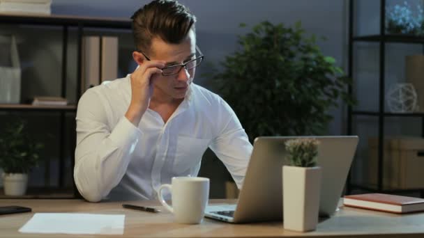 Portret van de jonge zakenman in casual shirt proberen werken met anoying hoofdpijn ter naar de laptop in het stijlvolle kantoor. — Stockvideo