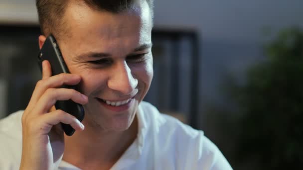 Νέοι επαγγελματίες άνθρωπος χρησιμοποιώντας έξυπνο τηλέφωνο για να μιλάμε με συνεργάτη στο παρασκήνιο γραφείο κατά τη διάρκεια της ημέρας εργασίας το βράδυ. Πλάγια όψη. — Αρχείο Βίντεο