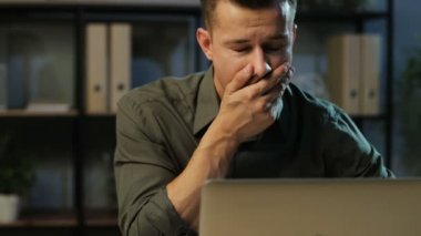 Yorgun iş adamı şık ofis içinde belgili tanımlık laptop üzerinde çalışıyor ve akşam saat sırasında esneme haki gömlek.