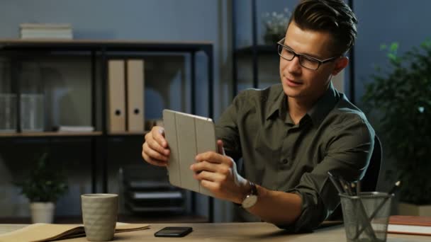 Hombre de negocios guapo utilizando la tableta para el chat de vídeo con amigos en la oficina por la noche . — Vídeos de Stock