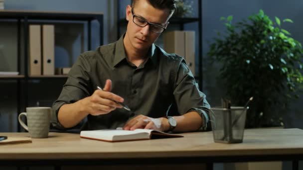 Hombre de negocios de confianza haciendo algunas notas en el libro de notas durante la noche en la oficina moderna . — Vídeos de Stock