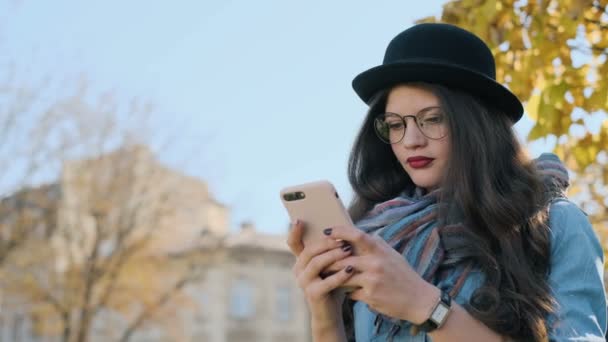 Retrato de hermosa chica turística utilizando el teléfono inteligente al aire libre. Mujer utilizando la aplicación en el teléfono inteligente fondo de la ciudad de otoño . — Vídeos de Stock