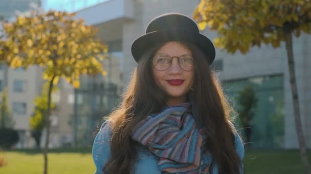 Retrato de cerca de una mujer sonriente mirando a la cámara. Chica joven mirando a la cámara en el fondo de la ciudad de otoño . — Vídeos de Stock