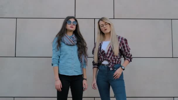 Meninas hipster alegres com óculos de sol se divertindo, soprando bolhas de doces bubblegum. Urbano, conceito de cidade. Fundo de parede — Vídeo de Stock