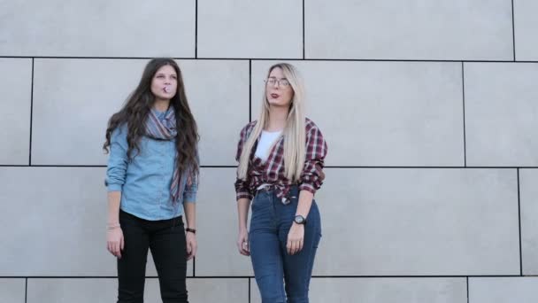 Chicas hipster alegre con gafas de sol que se divierten, soplando burbujas de caramelo de goma de mascar. Urbano, concepto de ciudad. Fondo de pared — Vídeos de Stock