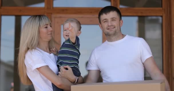 Happy married couple with little son arriving in new house. Buying real estate, mortgage, moving concept. Family with cardboard boxes in new house at moving day. — Stock Video