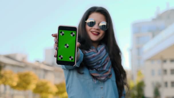 Mujer joven mostrando smartphone con pantalla verde. Muchacha joven atractiva mostrando el teléfono inteligente con croma-llave, pantalla verde — Vídeos de Stock