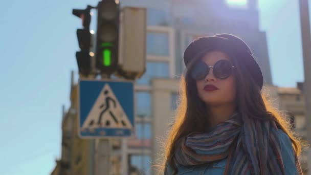 Portret van schattige hipster meisje close-up. Jonge vrouw verkleed zwarte hoed kijken camera en bril buitenshuis in de stad straat verkeerslicht achtergrond opstijgen. — Stockvideo