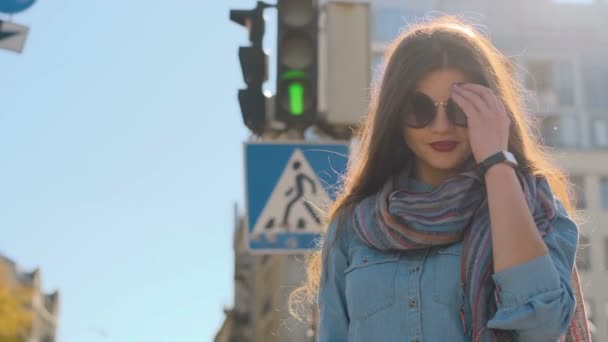 Närbild porträtt av söt hipster flicka. Ung flicka tittar kameran och tar bort glasögon utomhus i staden gatan trafikljus bakgrunden. — Stockvideo