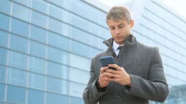 Cep telefonu kullaranarak çekici iş adamı. İşadamı kıyafetli akıllı telefon, meslektaşım, modern cam ofis binası arka plan için manifatura tutarak