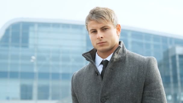 Atraktivní kavkazské podnikatel stál mimo sklo kancelářská budova. Obchodní koncept. Muž na sobě oblek a kabát, při pohledu na fotoaparát. — Stock video