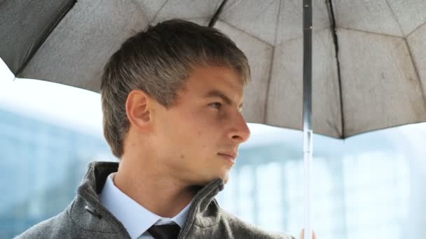 Портрет человека под черным зонтиком во время дождя. Серьезный бизнесмен в костюме и пальто, смотрит в камеру . — стоковое видео