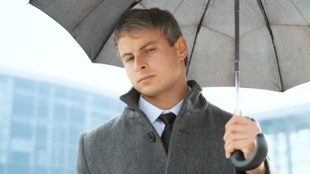 Σοβαρός επιχειρηματίας φορώντας κοστούμι και παλτό, βλέπουν φωτογραφική μηχανή κάτω από μαύρη ομπρέλα κατά τη διάρκεια βροχής. — Αρχείο Βίντεο