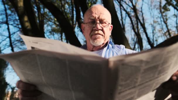 Aktif pensiun, pria senior dengan jenggot dan memakai kacamata membaca koran di taman . — Stok Video